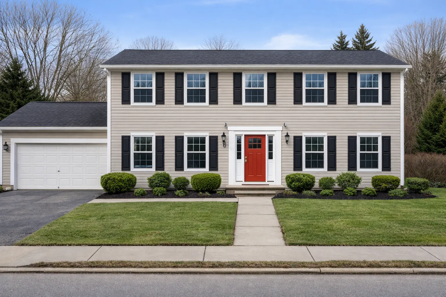 Updated colonial home exterior with black shutters, red front door, and fresh landscaping